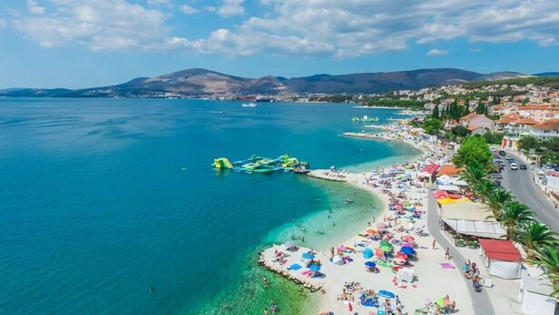 Une ville côtière dotée d’une plage, d’eaux d’un bleu limpide et bordée de montagnes.
