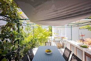 A covered outdoor dining area with a table set for two, surrounded by greenery and a white wall. - Studio Apartment with Terrace (Okrug Gornji)