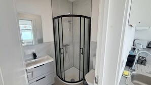 Moderni kylpyhuone, jossa on lasiseinällä varustettu suihku, valkoinen pesuallas peilillä ja wc-istuin.