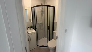 Moderni kylpyhuone, jossa on lasiseinällä varustettu suihku, wc ja peilillä varustettu pesuallas.