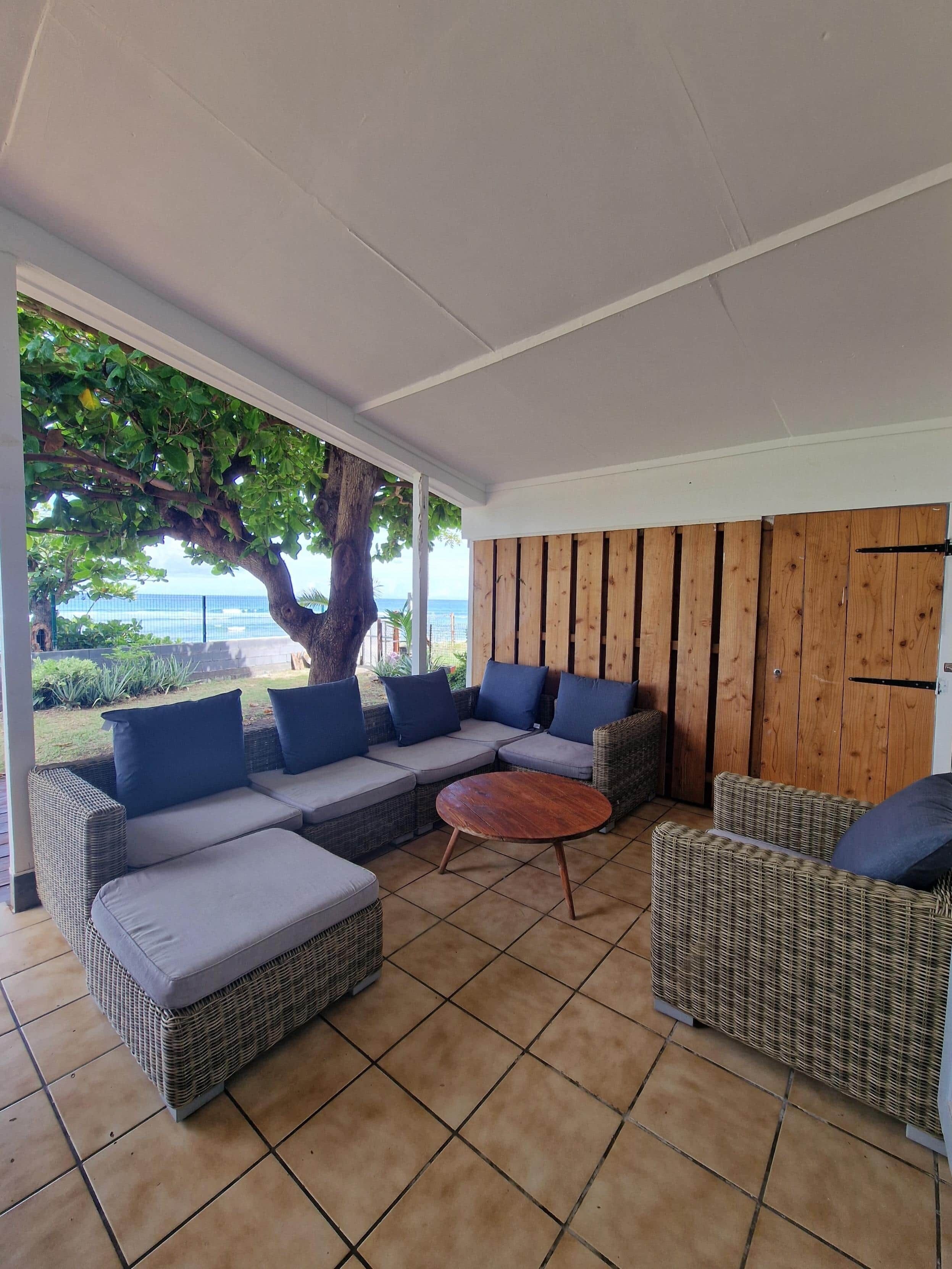 Un espacio de estar al aire libre cubierto con mobiliario de mimbre y vistas al mar.