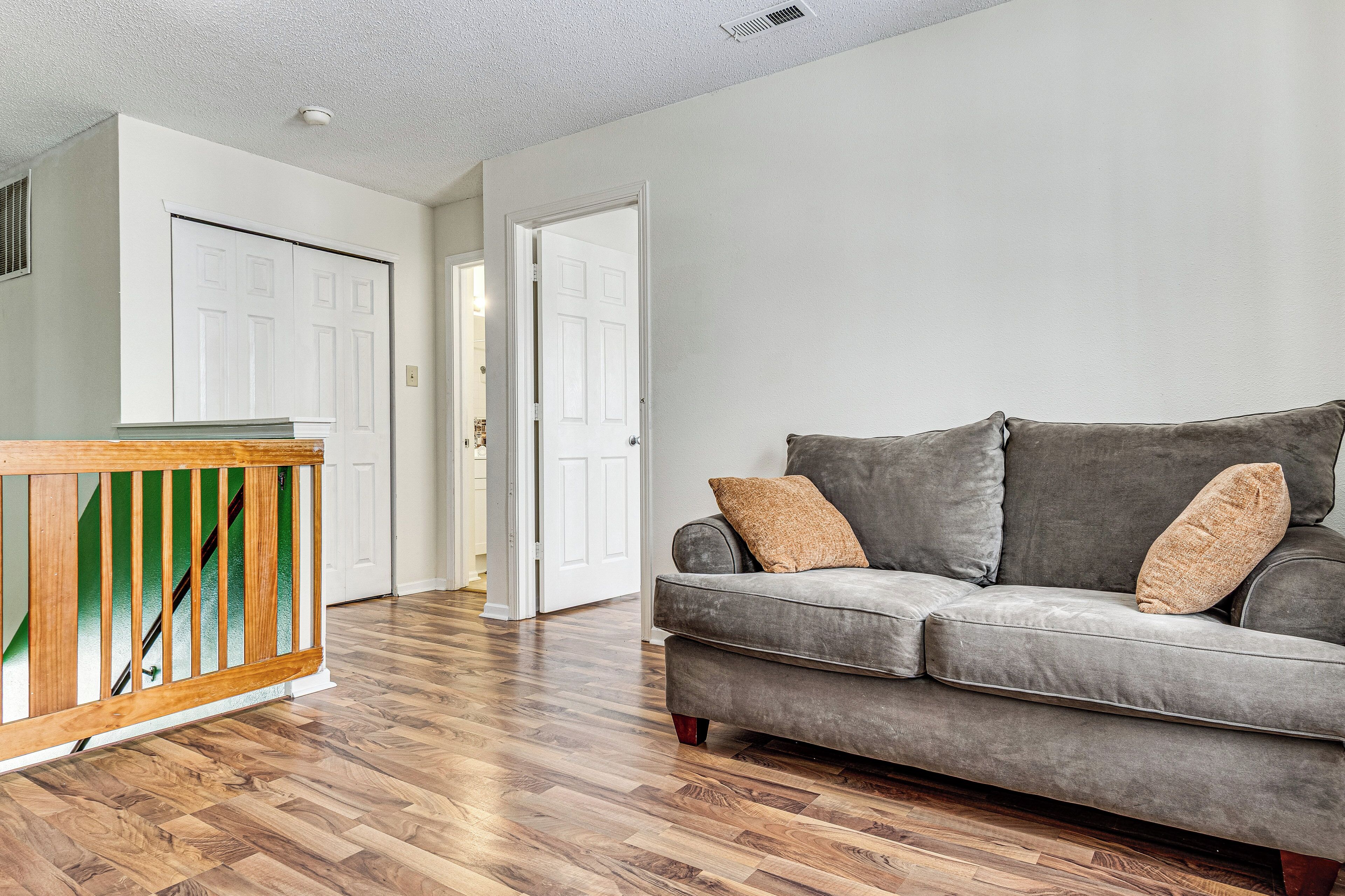 A living room with a grey sofa, wooden flooring, and a white door in the background.