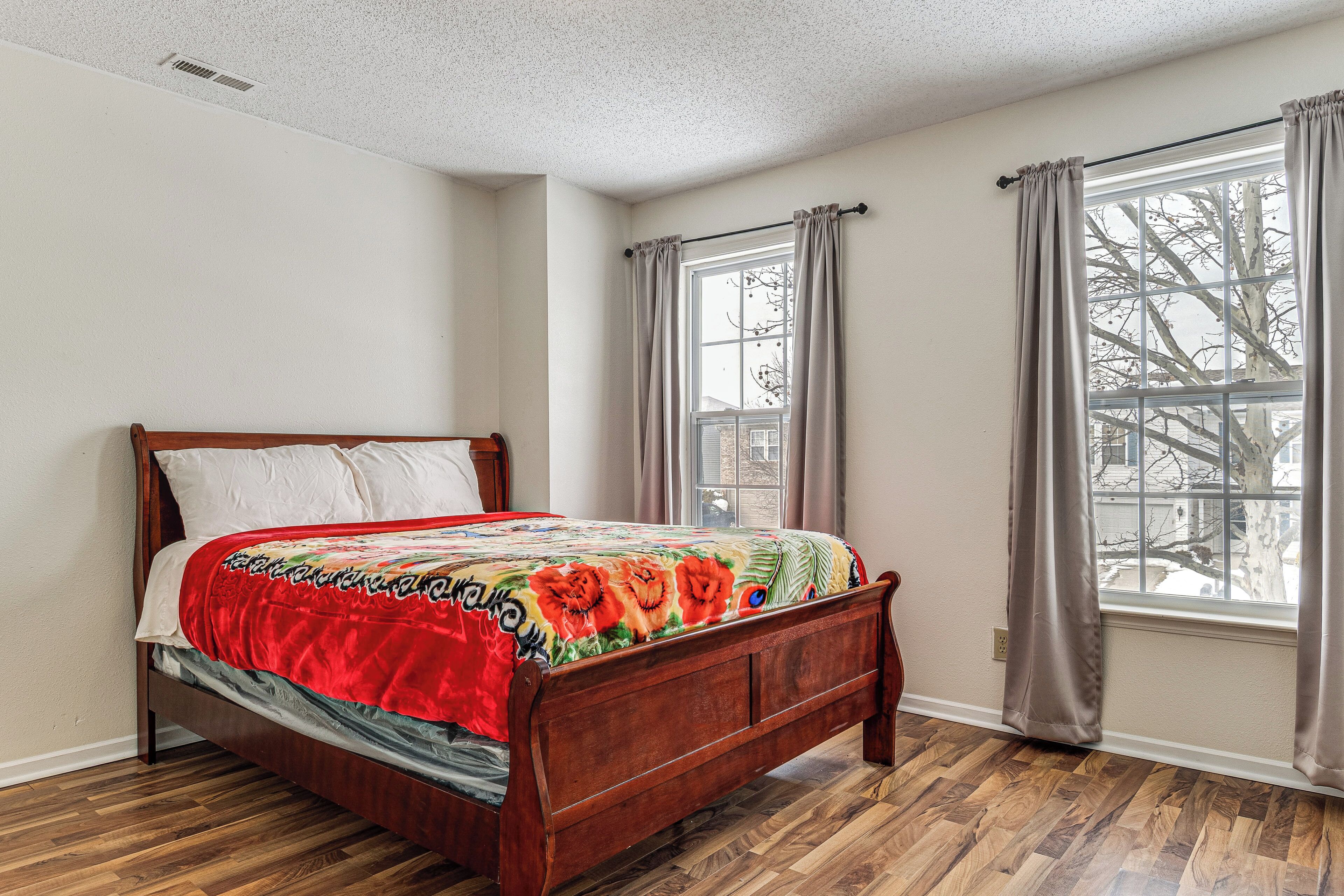 A bedroom with a wooden bed, a window with curtains, and a view of a tree outside.