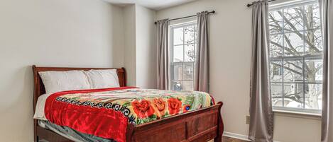 A bedroom with a wooden bed, a window with curtains, and a view of a tree outside.