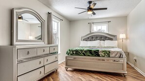 Een slaapkamer met een bed, een kaptafel, een plafondventilator en een raam.