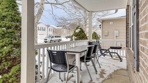Een overdekt terras met een witte reling, een tafel en vier stoelen.
