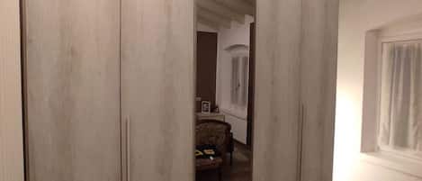 A room with a large wardrobe, wooden flooring, and a high ceiling with exposed beams.