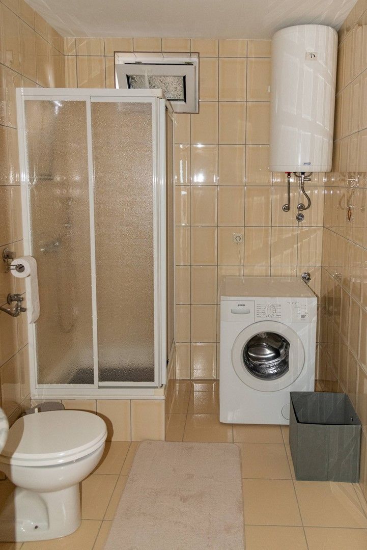A bathroom with a toilet, a shower enclosure, a washing machine, and a water heater.