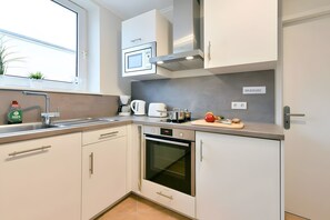 Una cocina moderna con armarios blancos, horno empotrado, microondas y cafetera.