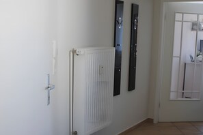 Un couloir avec un radiateur blanc, une porte dotée d’une poignée moderne et deux objets noirs verticaux accrochés au mur.