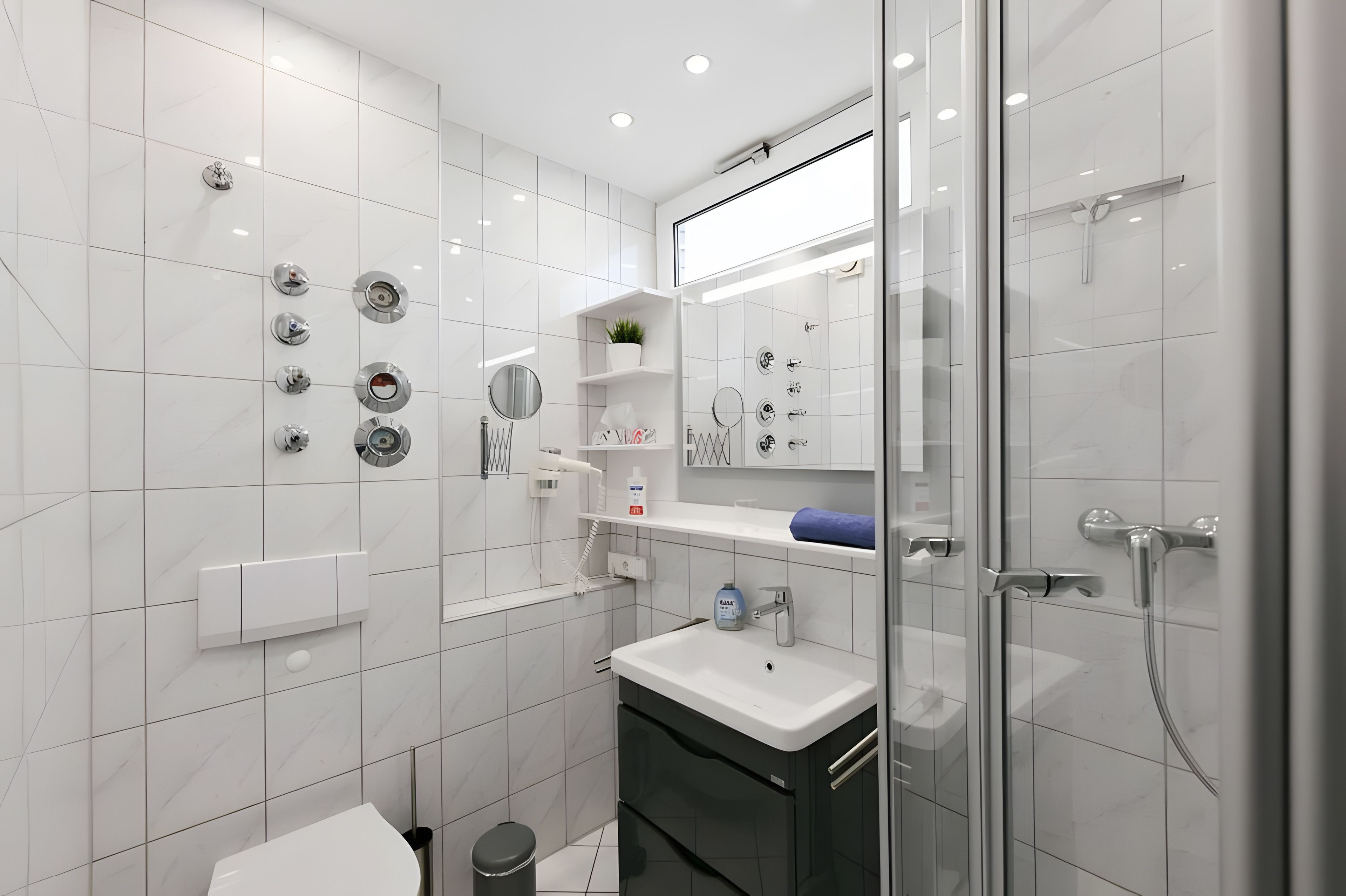 Ein modernes Badezimmer mit weißen Fliesen, einer Glasdusche, einem weißen Waschbecken und einem Spiegel.