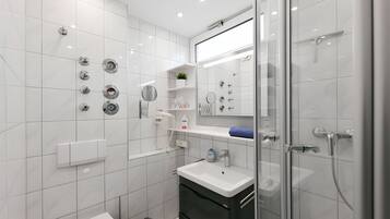 Ein modernes Badezimmer mit weißen Fliesen, einer Glasdusche, einem weißen Waschbecken und einem Spiegel.