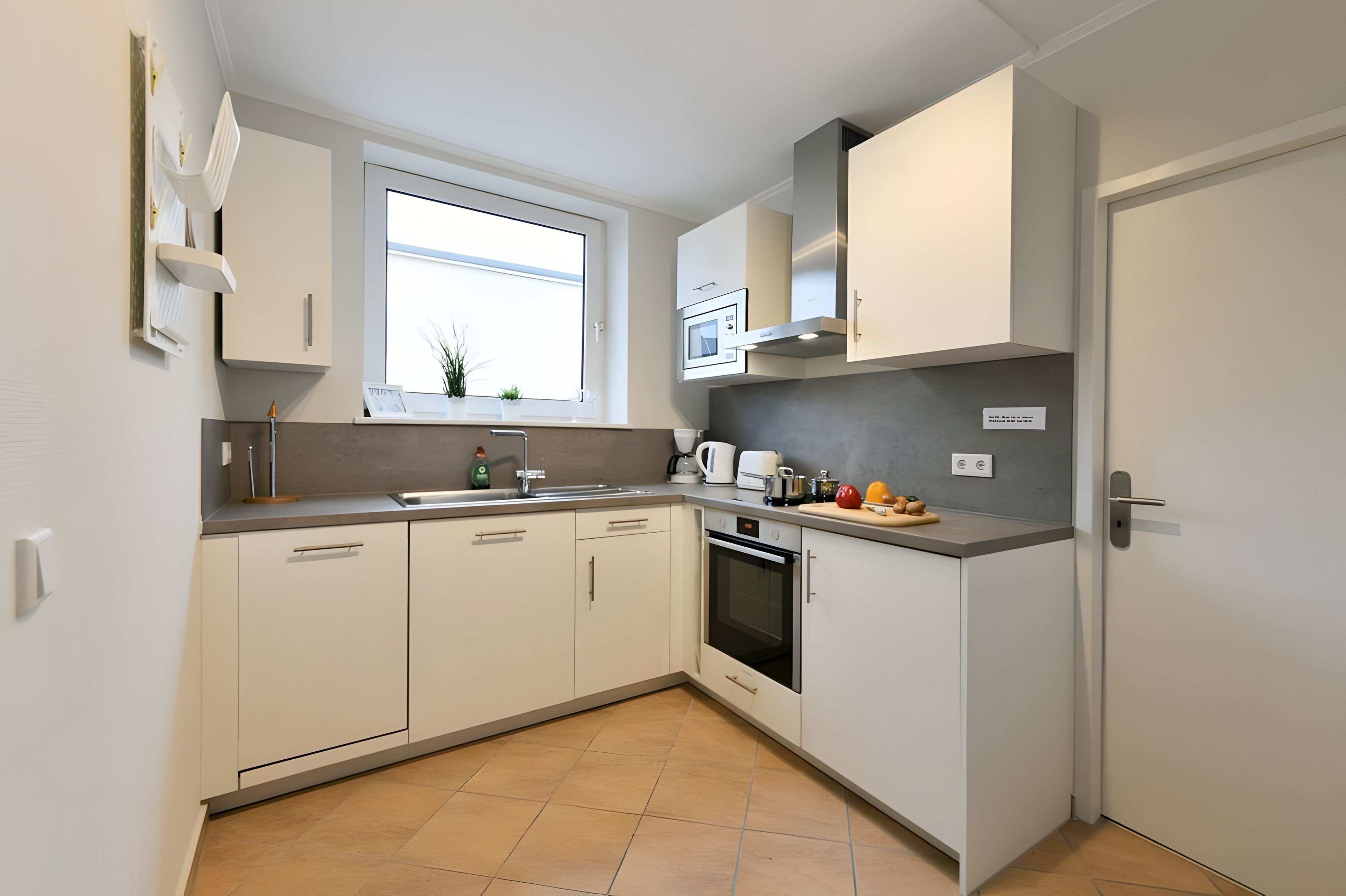 A modern kitchen with white cabinets, a built-in oven, and a window above the sink.