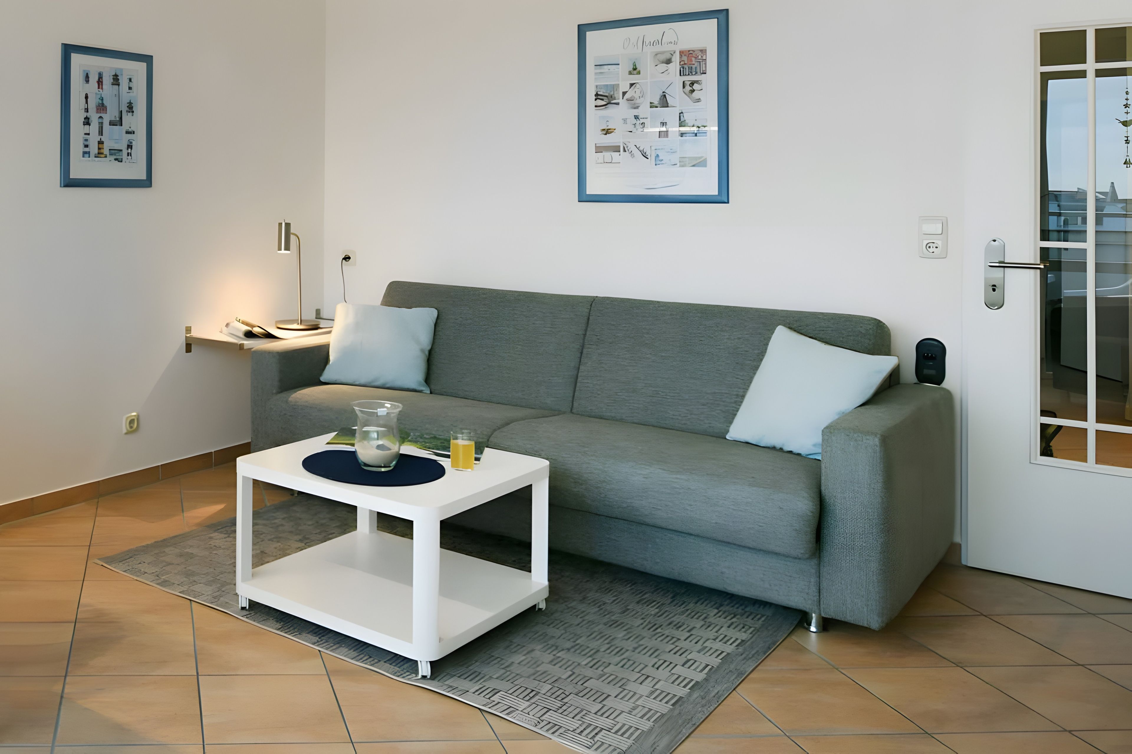 Ein modernes Wohnzimmer mit einem grauen Sofa, einem weißen Beistelltisch und einer Glas-Kanne auf dem Boden.