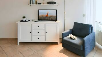 En moderne stue med et hvidt skab, en blå lænestol, et fjernsyn og en gulvlampe.