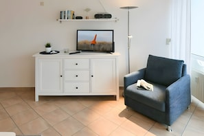 Una sala de estar moderna con un armario blanco, un sillón azul, un televisor y una lámpara de pie.