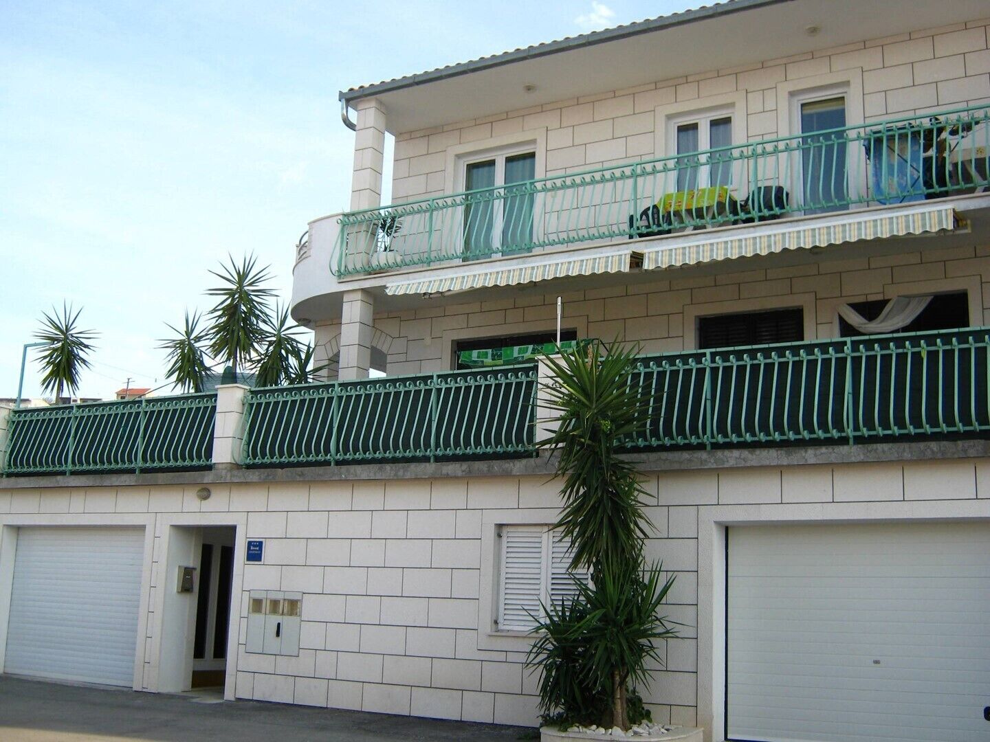 A two-story building with a white facade, a balcony with green railings, and a garage door.