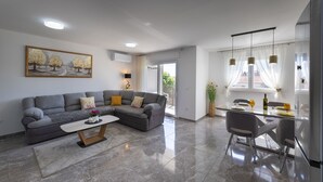 Una sala de estar moderna con un sofá seccional gris, una mesa de centro y un comedor con una mesa de vidrio y sillas.