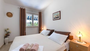 Ein ordentlich bezogenes Bett mit weißer und brauner Bettwäsche, ein Fenster mit Vorhängen, eine Nachttischlampe und ein gerahmtes Bild an der Wand.