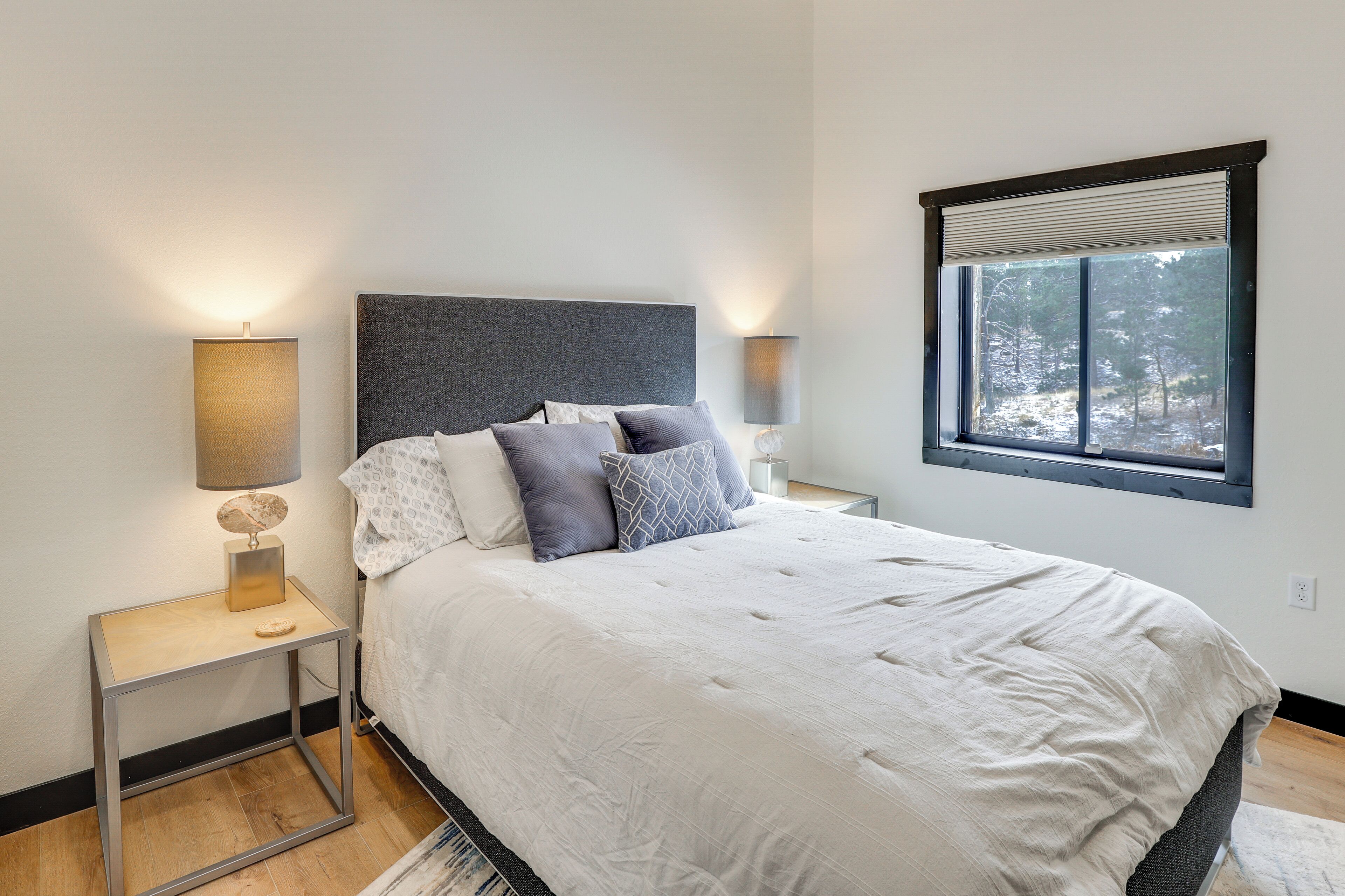 A modern bedroom with a large bed, two bedside tables, and a window with a view of trees.