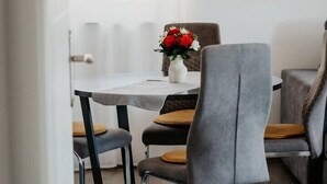 Ein moderner Essbereich mit einem runden Tisch, grau gepolsterten Stühlen und einer Vase mit roten Blumen.