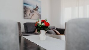 Eine weiße Vase mit roten und weißen Blumen auf einem Tisch in einem Wohnzimmer mit grauen Sofas und einem Bild an der Wand.