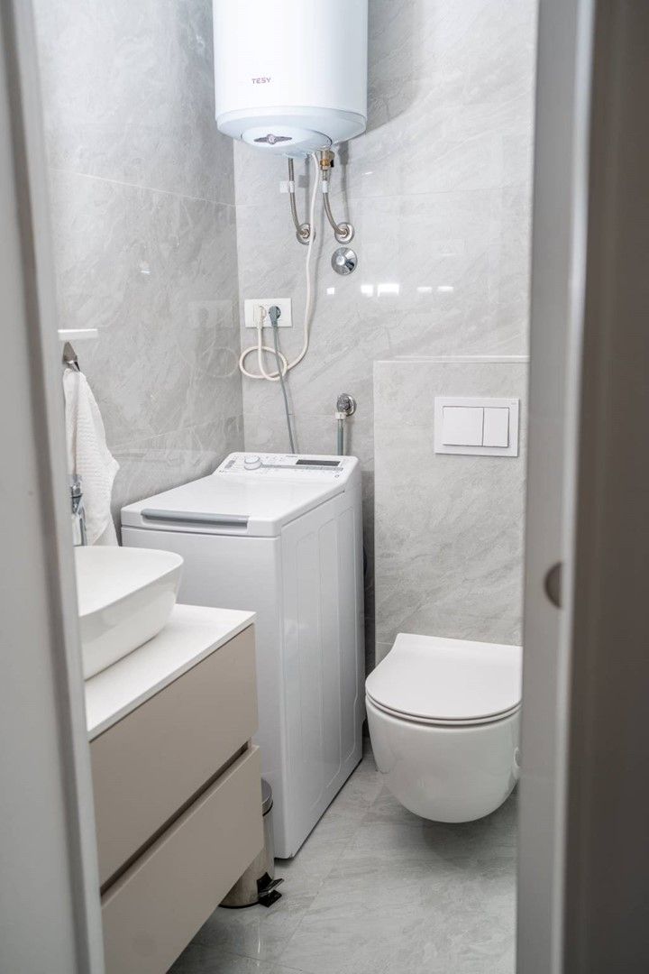 Un baño pequeño con lavadora incorporada, inodoro y lavamanos.