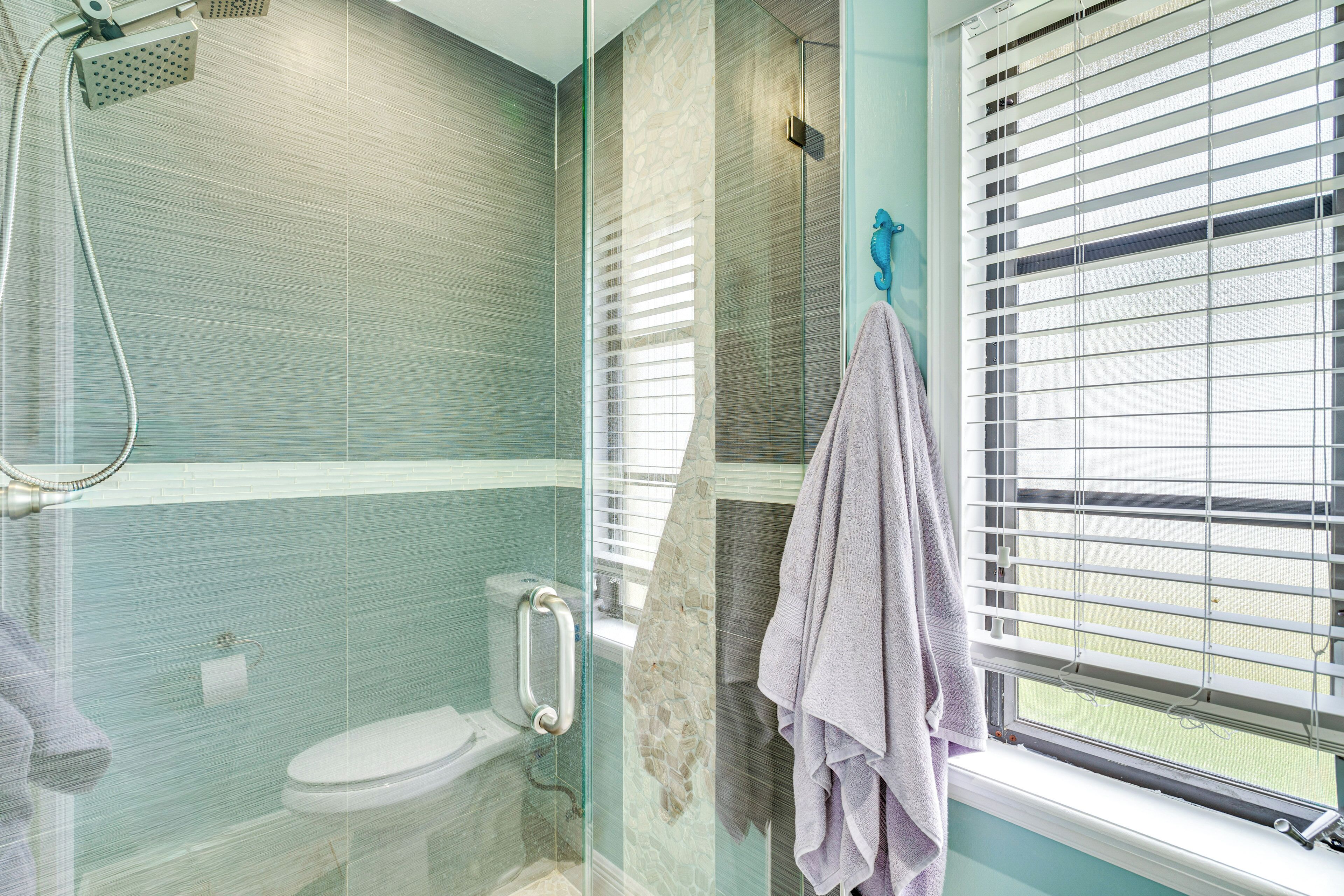 Un baño con cabina de ducha de vidrio, inodoro y ventana con persianas.