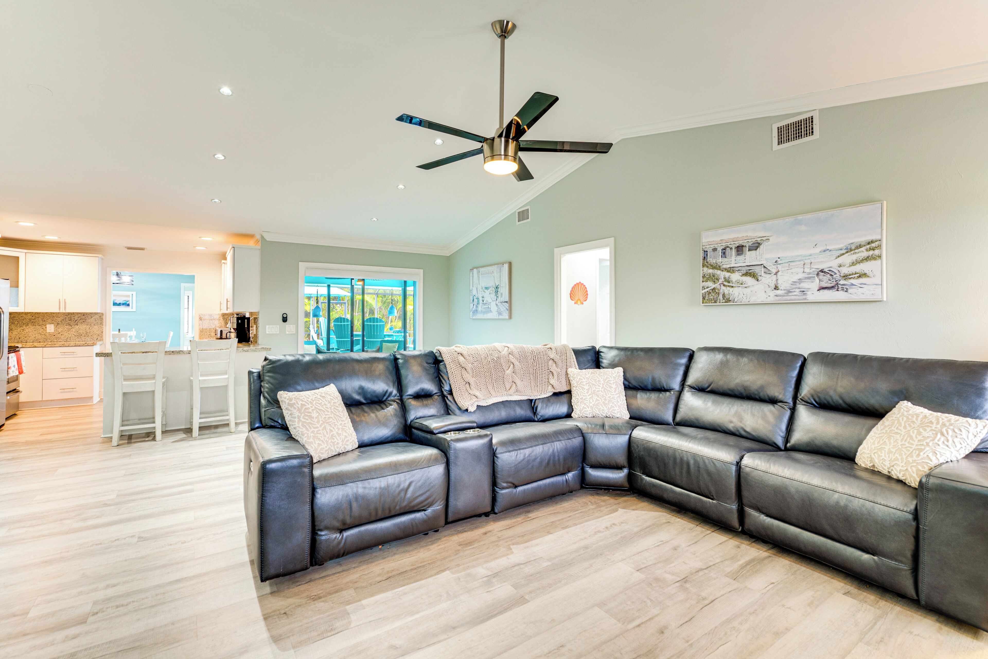 A modern living room with a sectional sofa, a ceiling fan, and a kitchen in the background.