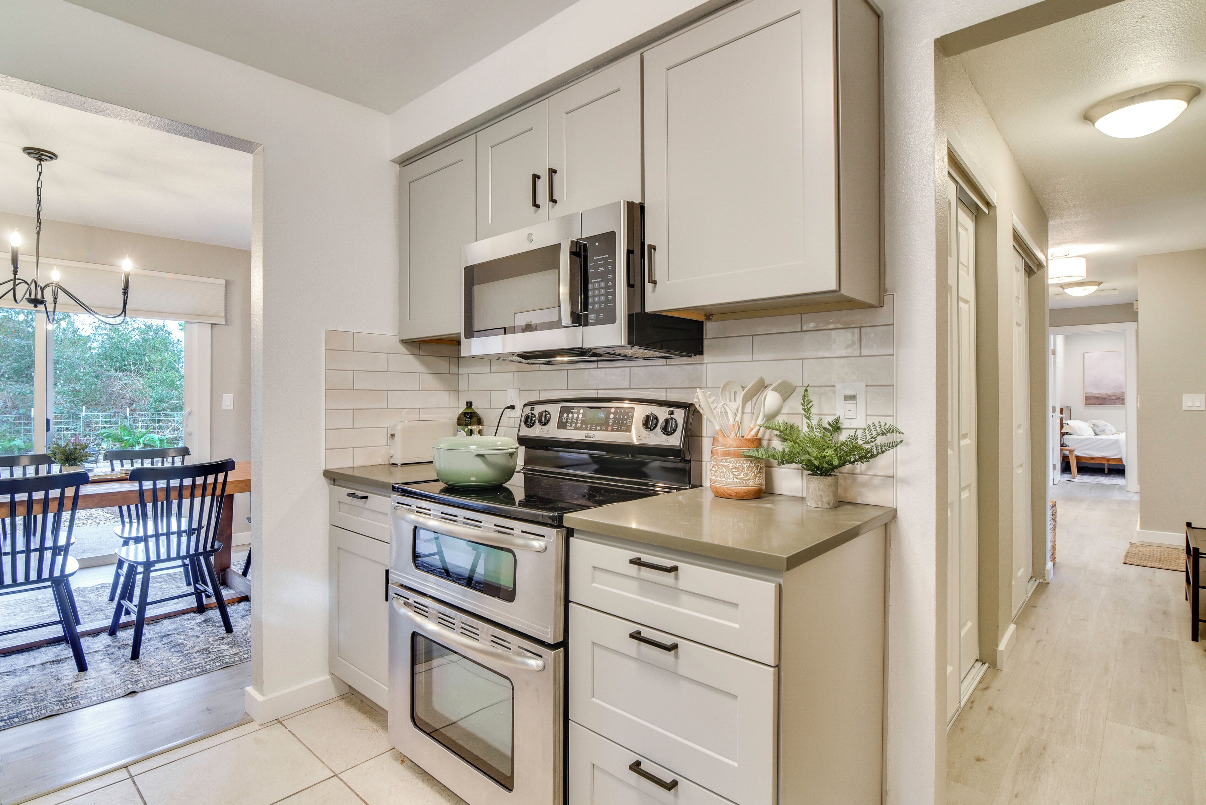 A modern kitchen with a built-in microwave, oven, and sink, a dining area with a table and chairs, and a view of the outdoors through a window.