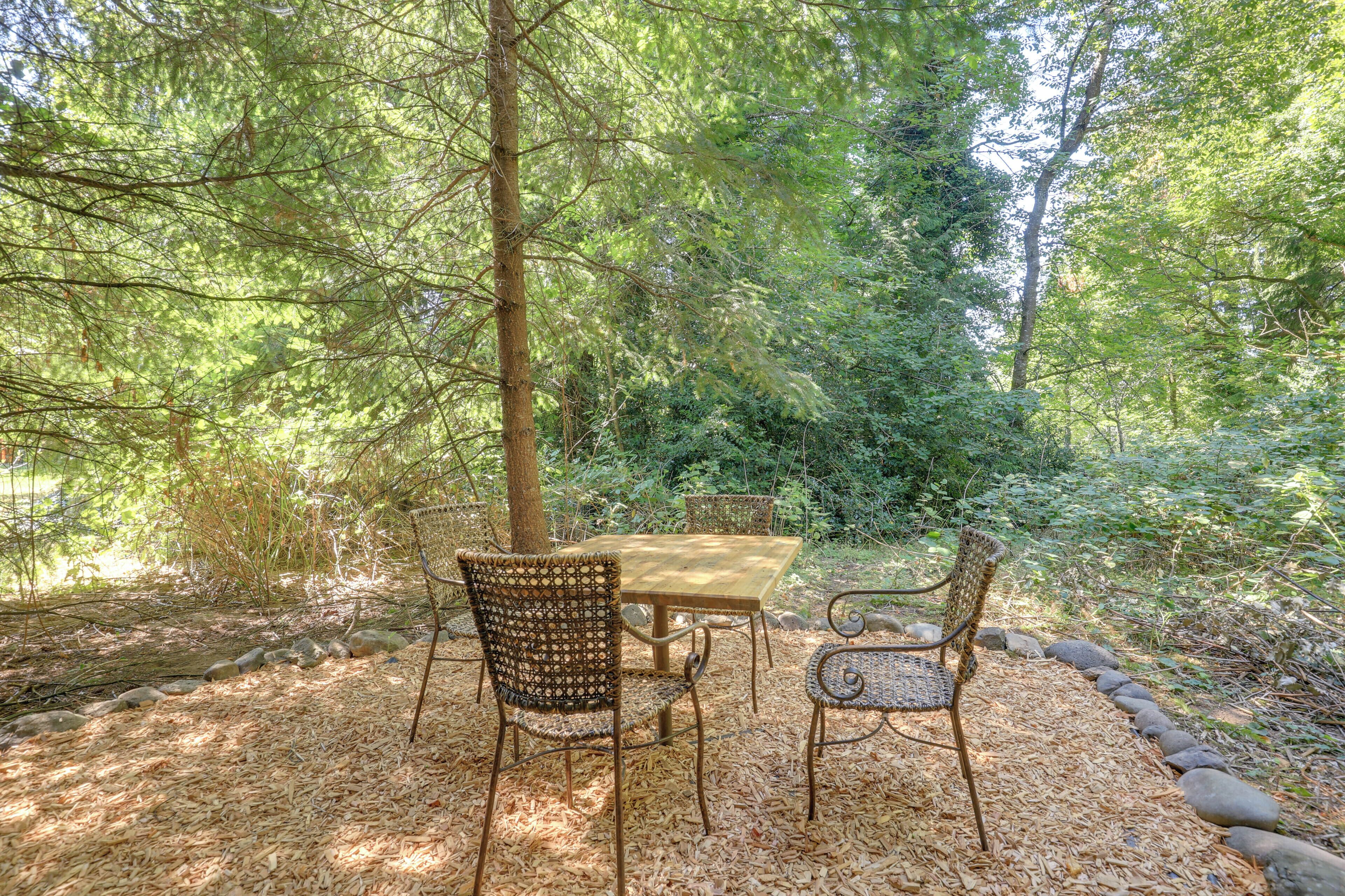 An outdoor seating area with a table and chairs, surrounded by trees and natural foliage.