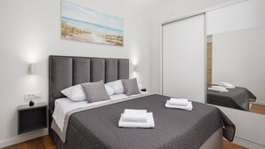 A modern bedroom with a large bed, a bedside table, a nightstand, a wall-mounted light, a painting, and a mirror. - Two Bedroom Apartment (Kaštel Sućurac)