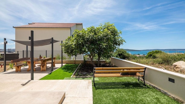 A rooftop terrace with a wooden bench, a small tree, and a view of the sea. - Two Bedroom Apartment (Kaštel Sućurac)