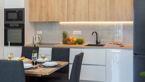 A modern kitchen with wooden cabinets, a built-in microwave, a sink, and a dining area with a table set for two. - Two Bedroom Apartment (Kaštel Sućurac)