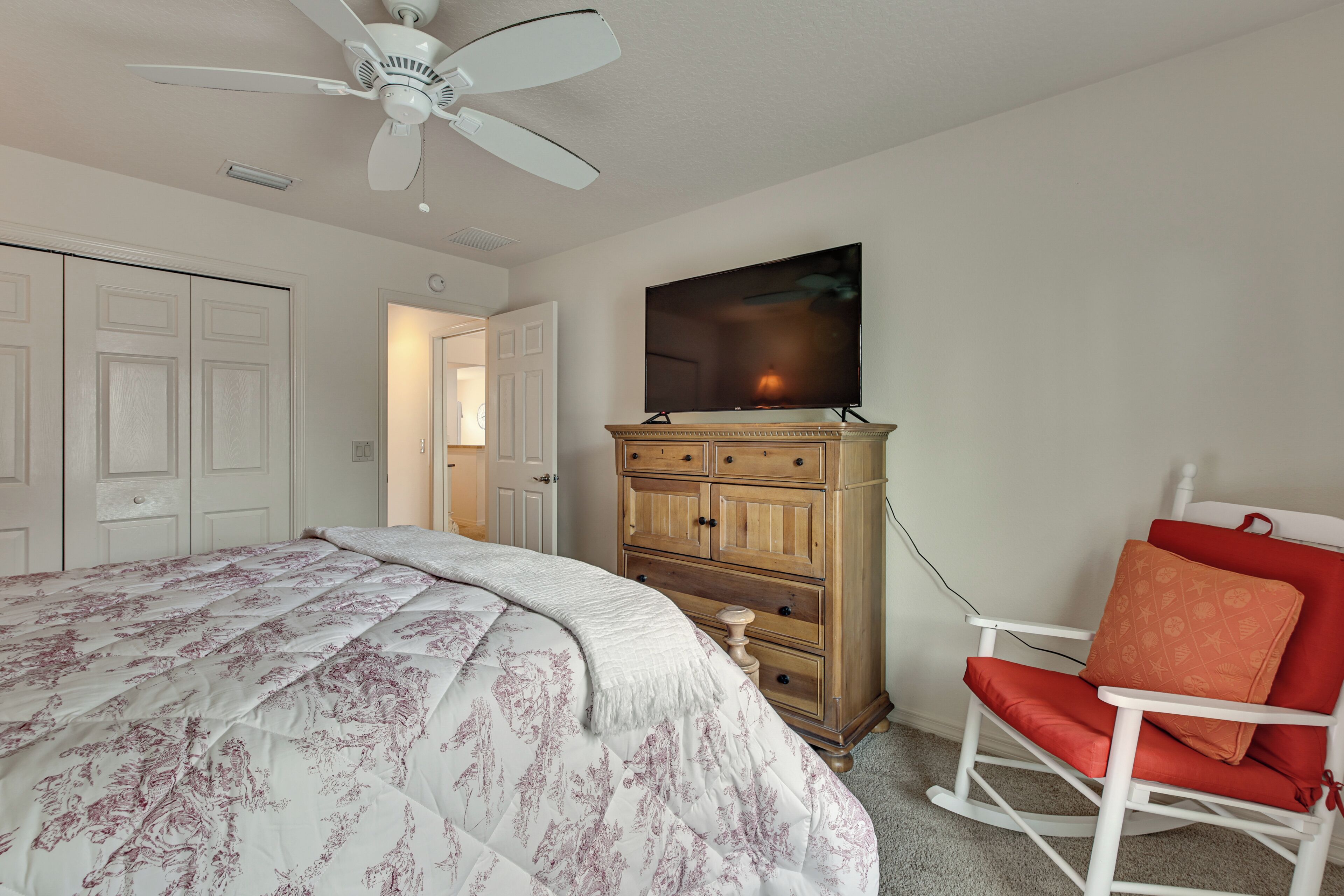 Een slaapkamer met een bed, een dressoir, een televisie en een schommelstoel.