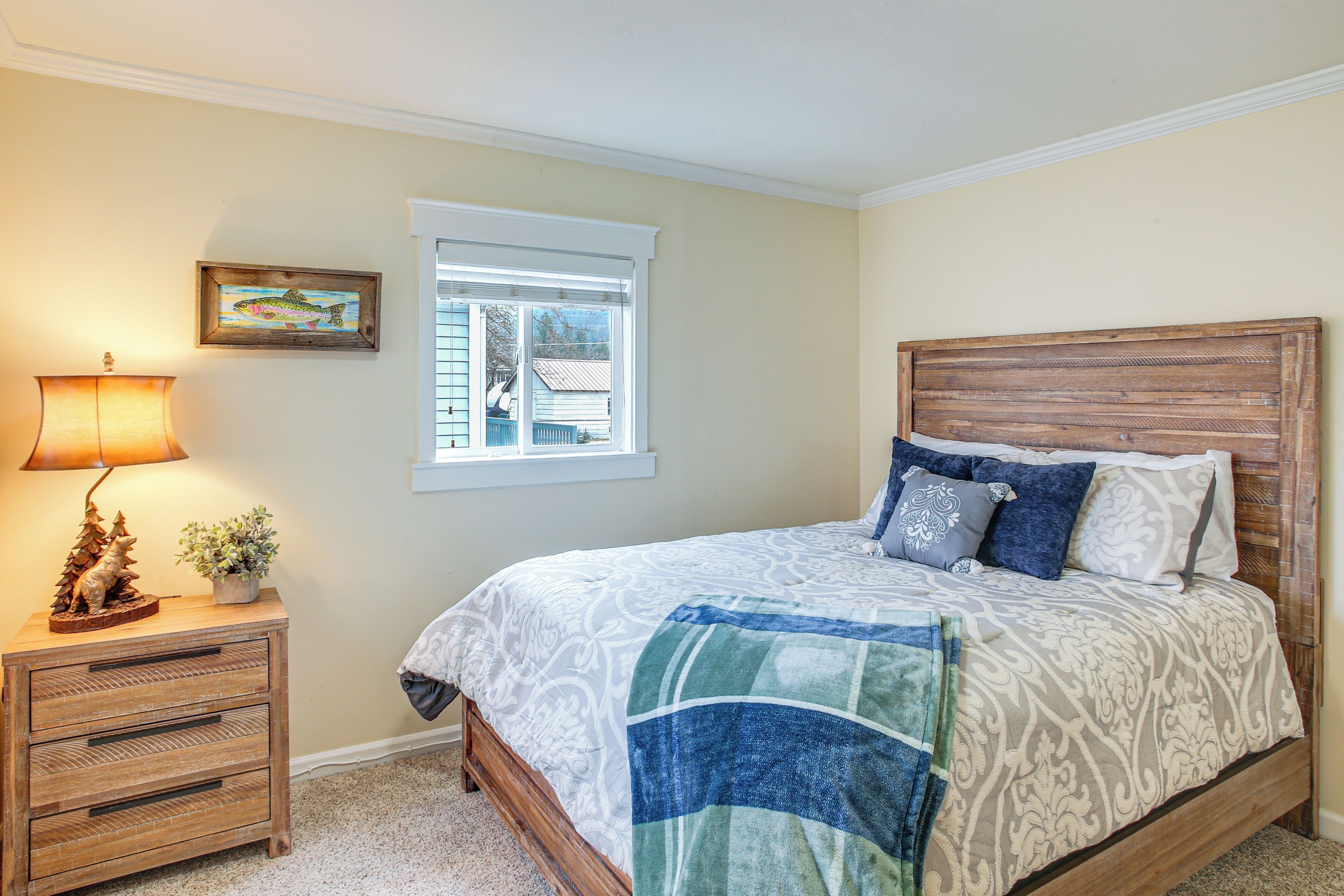 A bedroom with a bed, a nightstand, a lamp, a window, and a picture on the wall.