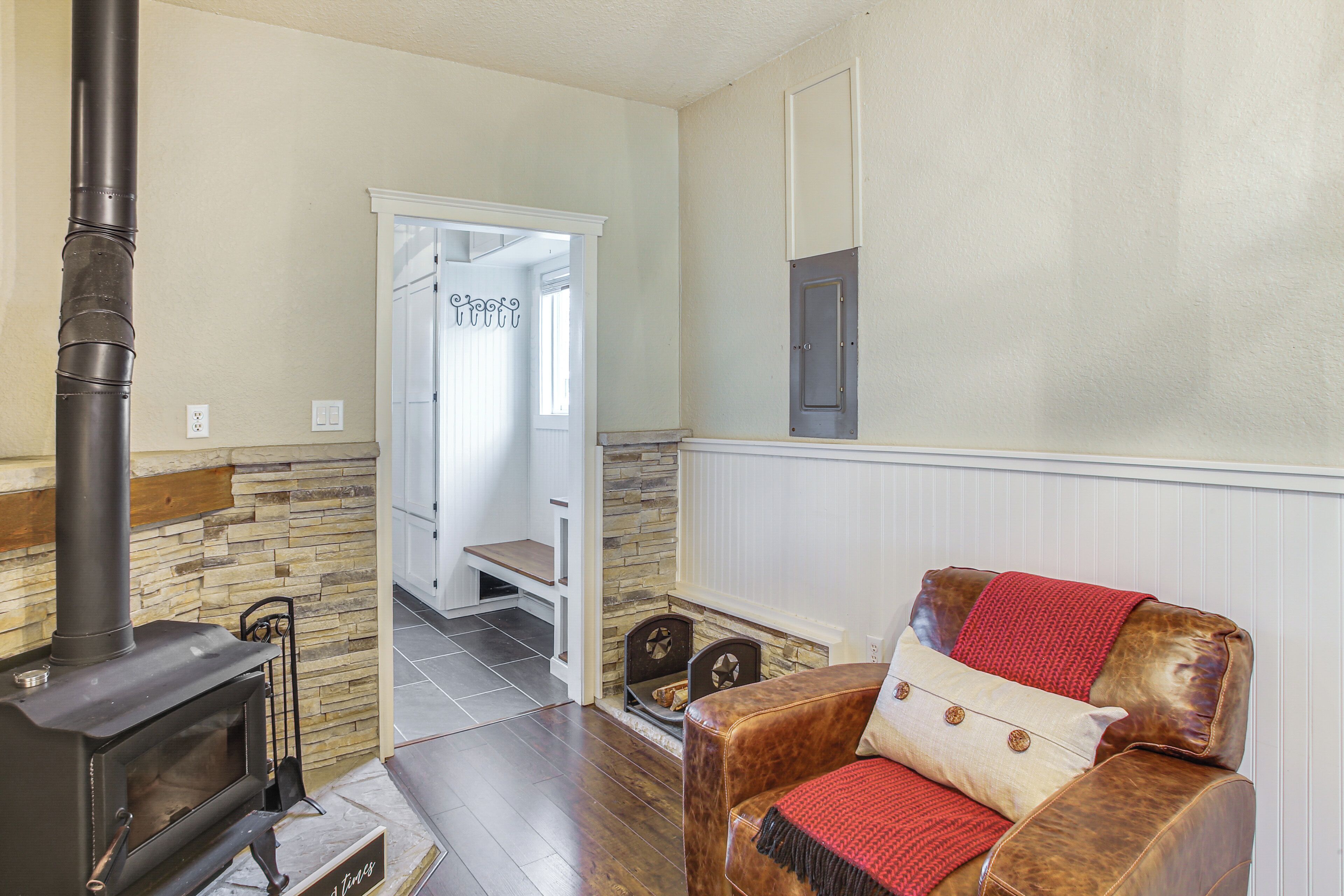Un salon chaleureux avec un poêle à bois, un canapé en cuir recouvert d’un plaid rouge et un mur en pierre.