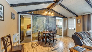 A cozy room with a wooden dining table, a sofa, and a view of a bedroom through a glass door. - Deck & Fire Pit! Muskingum Fishing Cabin (Dresden)