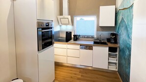 Una cocina compacta con horno integrado, cafetera y ventana con persianas.