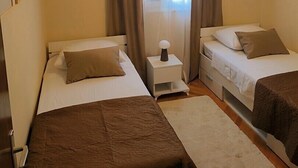 Una habitación con dos camas, una mesita de noche, una lámpara y una ventana con cortinas.