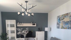 Una sala moderna con un sofá gris, una mesa de comedor redonda con cuatro sillas, un armario blanco y una lámpara del techo.