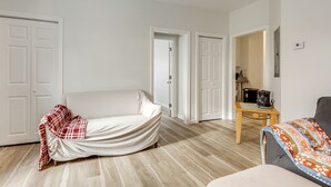 Een kamer met een witte bank, een kleine tafel met een koffiezetapparaat, en een grijze stoel.