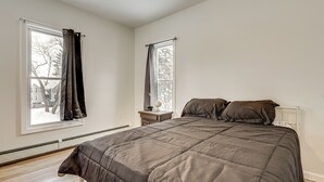 Een slaapkamer met een groot bed, twee ramen, een nachtkastje en een radiator.