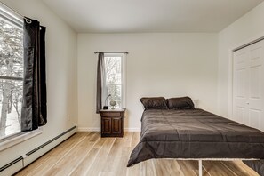 Um quarto com cama, mesa de cabeceira, janela com cortinas e porta.