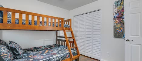 Una cama individual superpuesta con escalera, un armario con puertas correderas y un ventilador de techo.