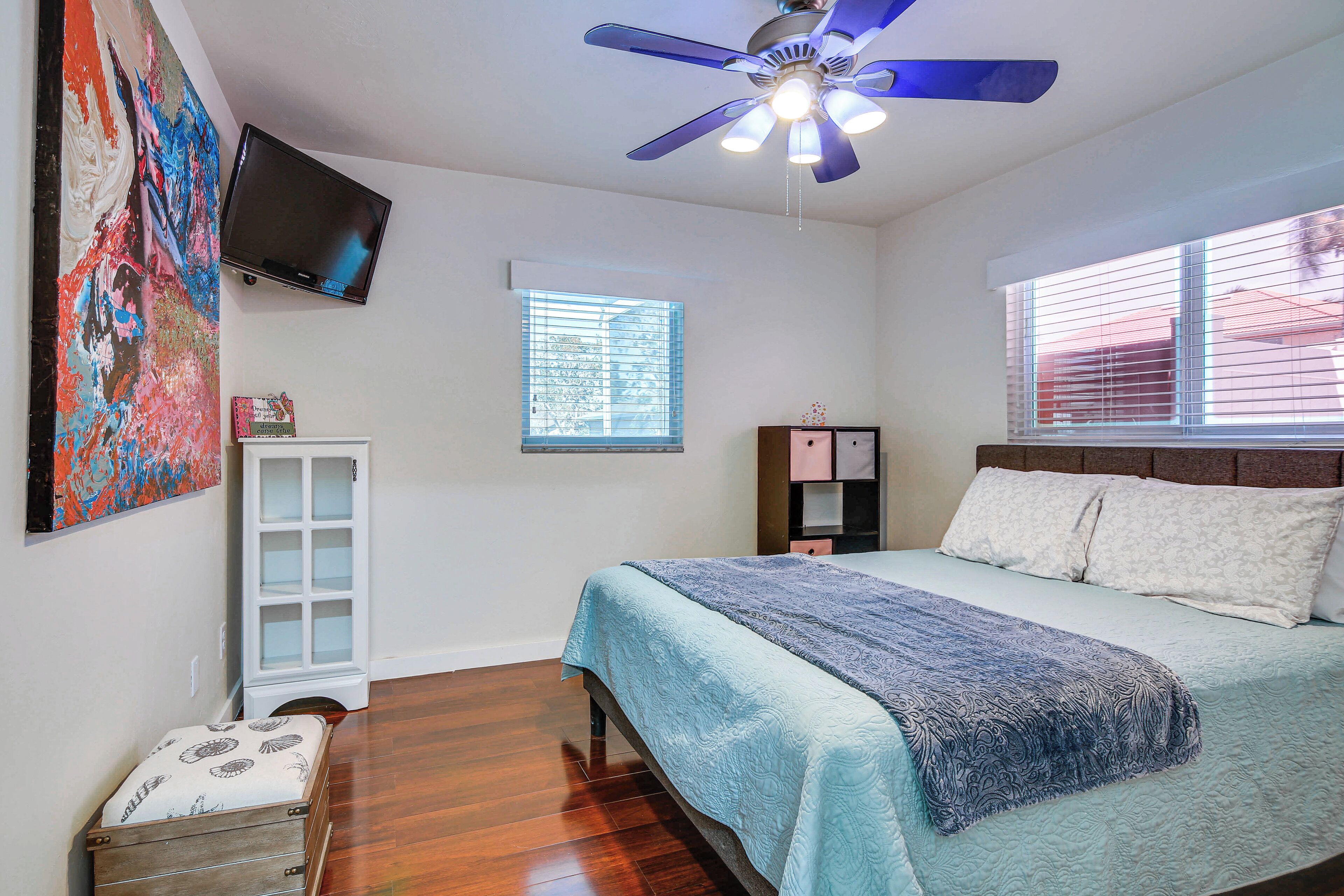 A bedroom with a bed, a ceiling fan, a TV, a window, and a cabinet.