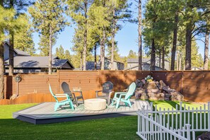Un patio trasero con terraza de madera, mobiliario exterior, cerca blanca en espiga y elemento decorativo de piedra.
