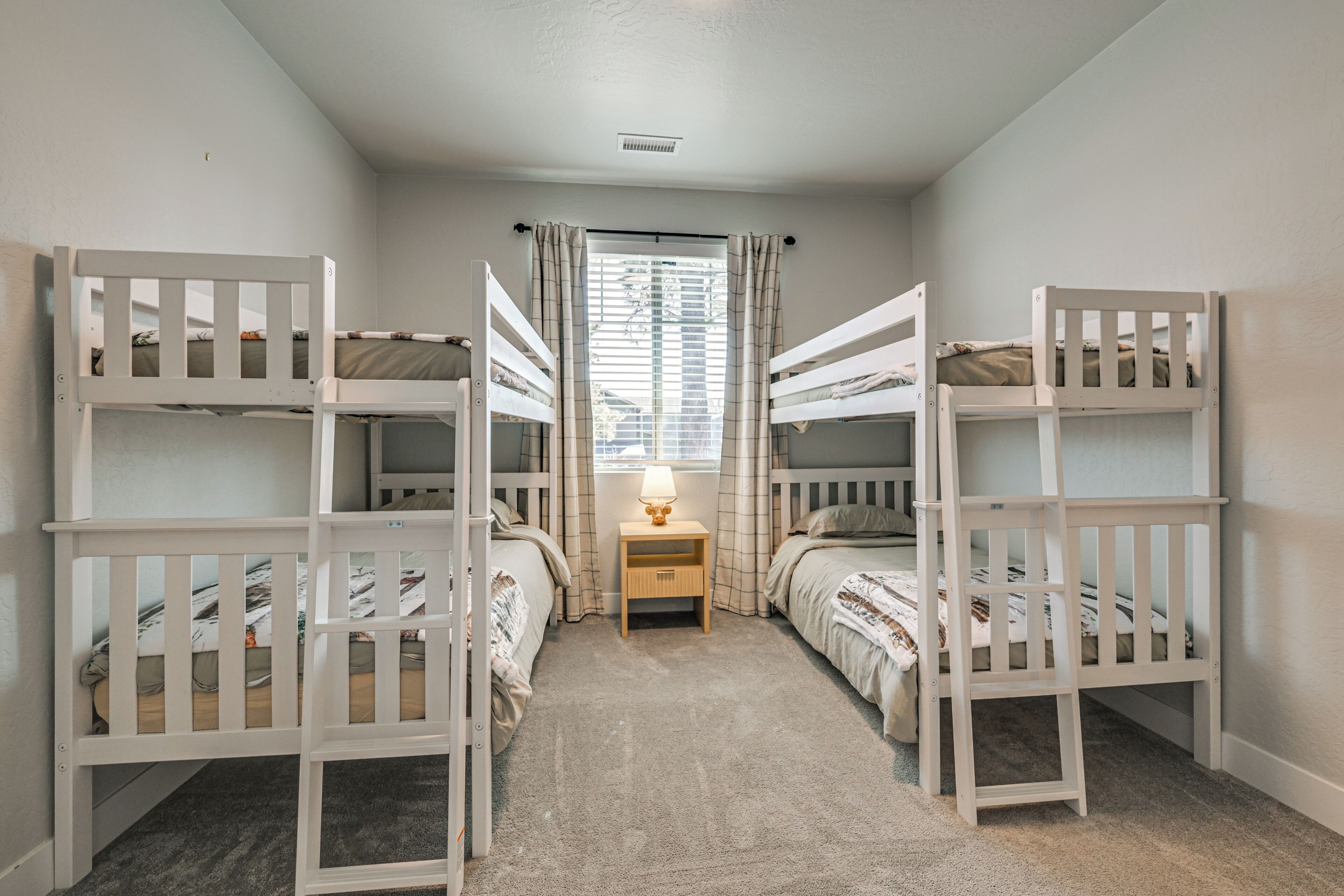 A room with bunk beds, a small bedside table with a lamp, and a window with curtains.