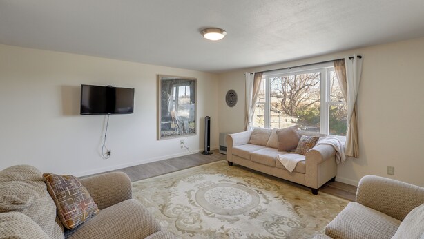 A living room with a beige sofa, a patterned rug, a flat-screen TV, and a window with curtains.