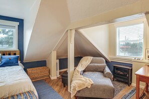 A cozy attic bedroom with a sloped ceiling, a bed, a chair, a small table, and a wood-burning stove. - Work & Play in Walkable Midtown Coeur D'alene! (Coeur d'Alene)